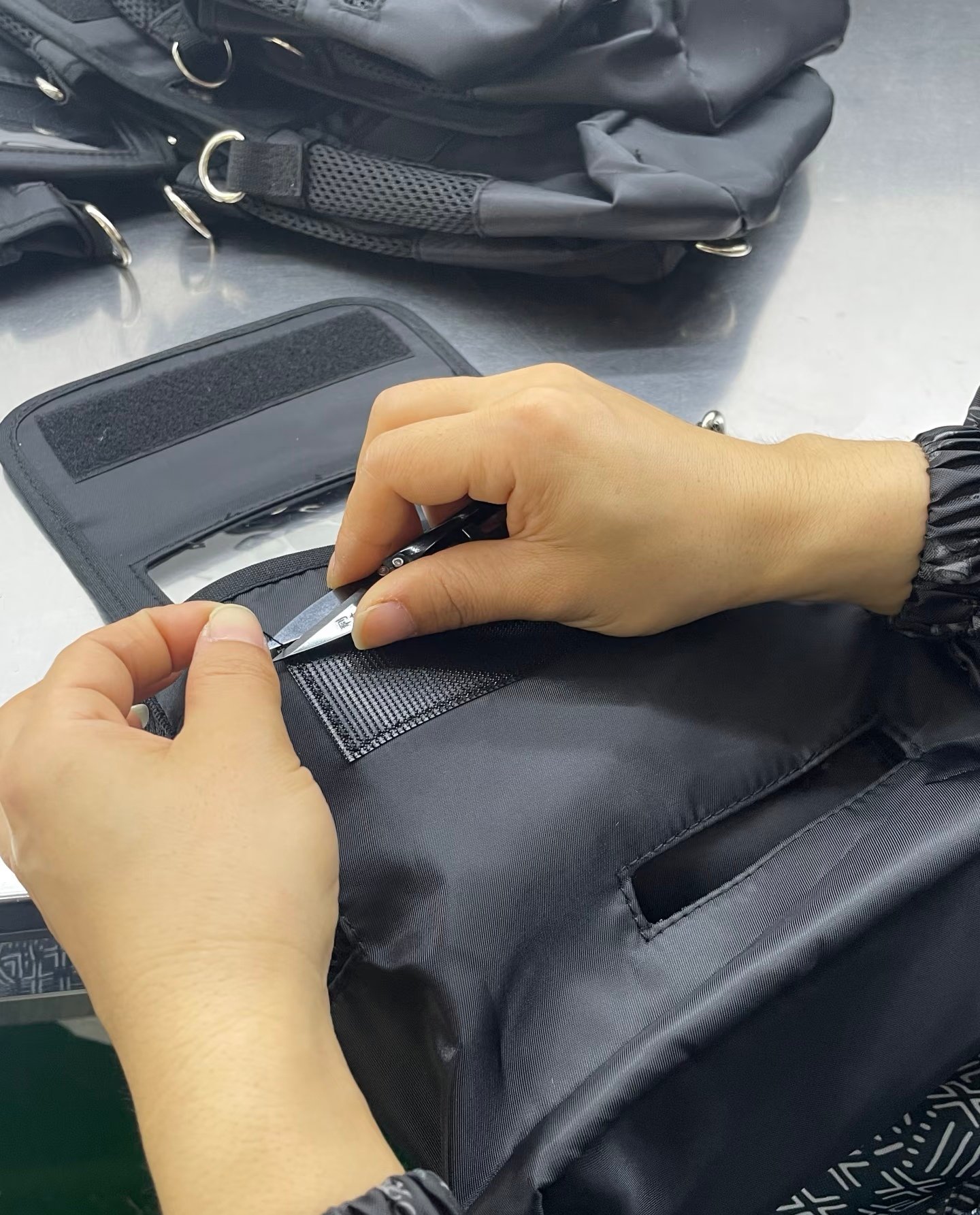 Inspector checking and trimming stitching on a black backpack strap