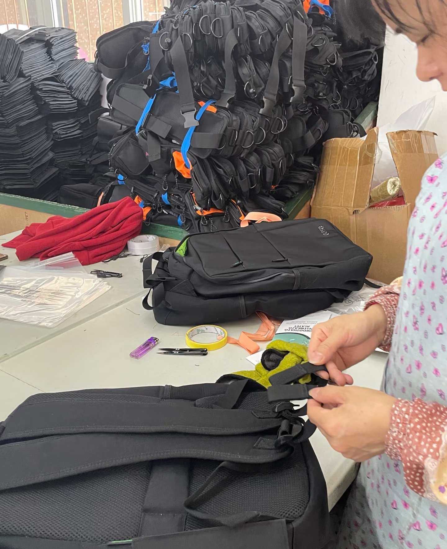 Worker inspecting straps and fittings on finished black backpacks