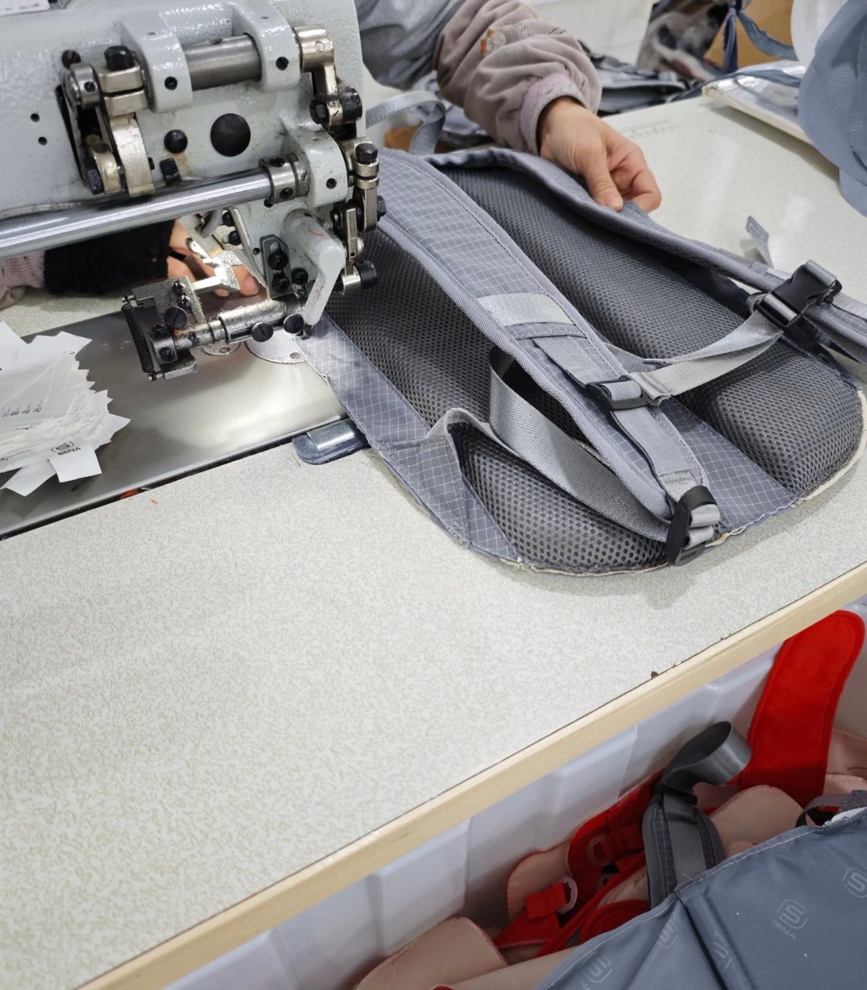 Worker sewing and assembling a grey backpack in the Baigouledao factory